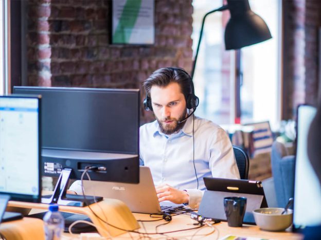 Professional working on his computer, wearing a headset, analyzing data, reflecting business intelligence and data-driven decision-making.